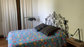 Une chambre avec une couvre-lit à motifs floraux, une tête de lit en métal, une table de chevet avec une lampe et un portant à vêtements.