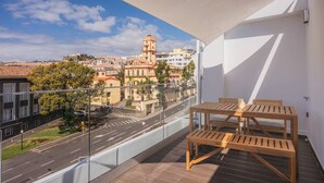 A balcony with a wooden table and chairs, offering a view of a historic tower and surrounding buildings. - Rooftop Studio Ocean & City View (Funchal)