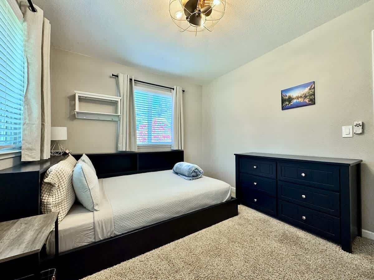 A bedroom with a bed, bedside tables, a dresser, a window with blinds, and a ceiling fan.