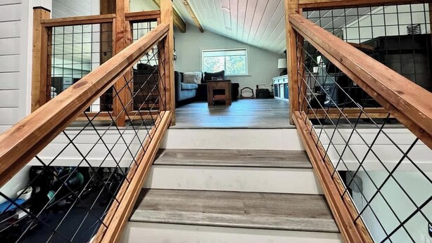Un escalier avec des rampes en bois et une grille métallique, menant à un espace de vie comprenant un canapé et une fenêtre.