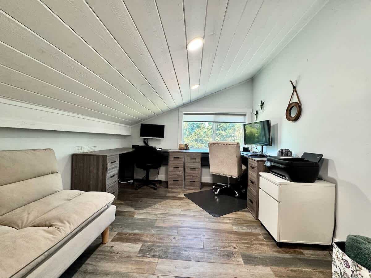 A compact living space with a sofa, a desk, a chair, a TV, and a printer.
