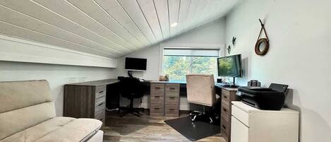 A compact living space with a sofa, a desk, a chair, a TV, and a printer.