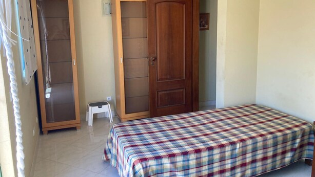 Un dormitorio con una cama, un armario y un taburete pequeño.