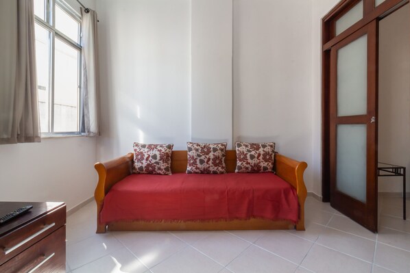 Quarto com sofá de madeira, colcha vermelha e armário de madeira.