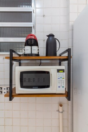 Een keuken met een magnetron op een plank, een koffiezetapparaat en een waterkoker.