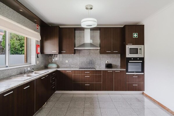 Una cocina moderna con armarios de madera oscura, encimeras de granito, campana extractora de acero inoxidable, microondas y horno.