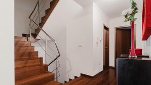 Una escalera de madera con barandilla de metal, pared blanca y un florero rojo con flores sobre una mesa negra.