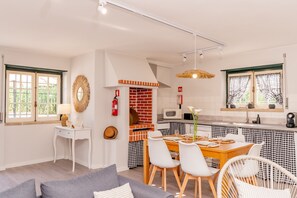 Une cuisine moderne avec un four en briques, des meubles blancs et un coin repas agrémenté d’une nappe à carreaux.