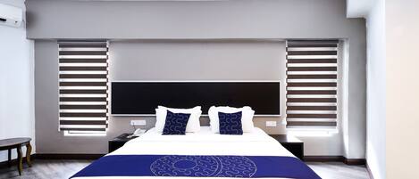 A modern hotel room with a large bed, a flat-screen TV, and a window with blinds.