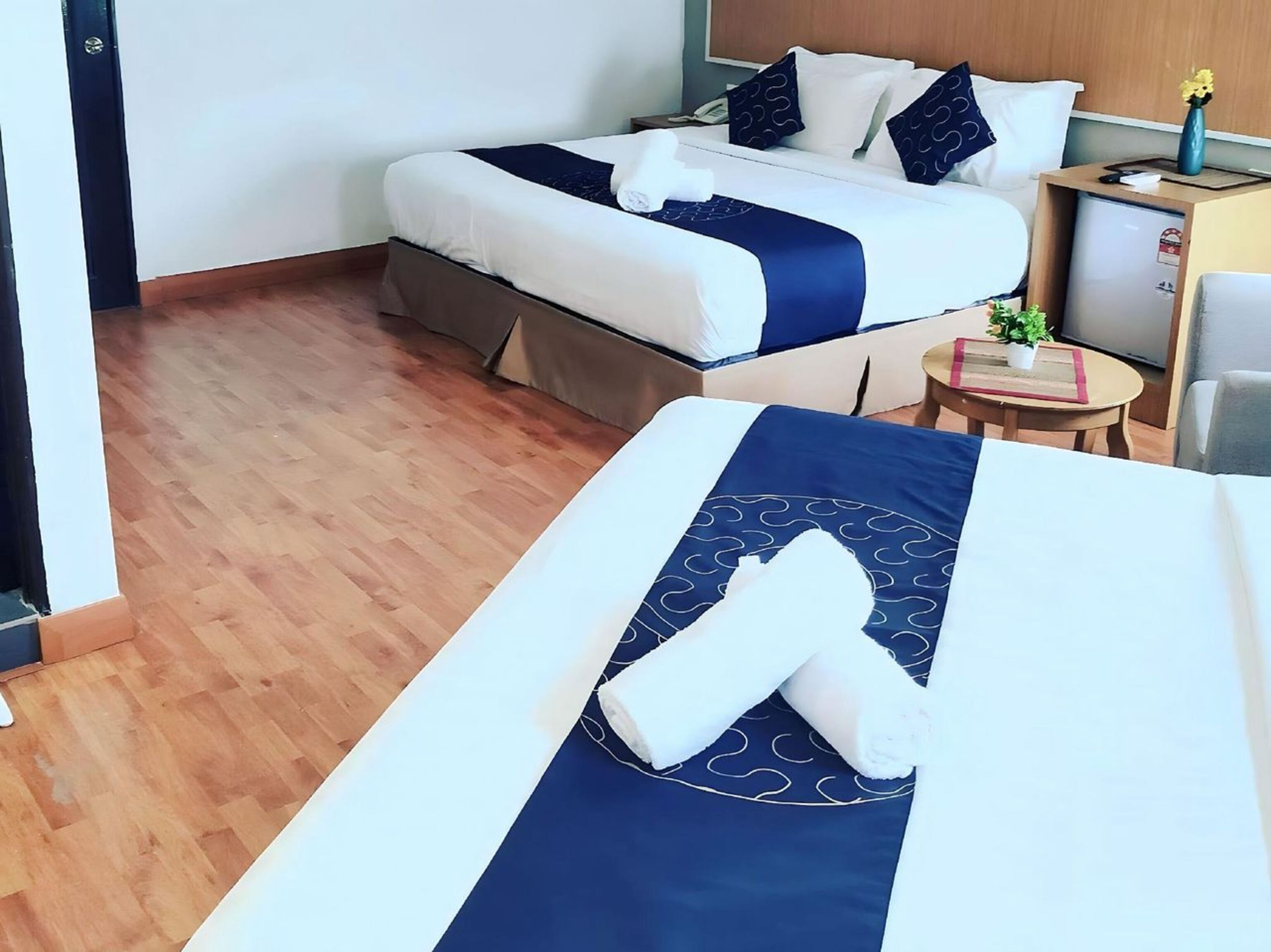 Une chambre d’hôtel avec deux lits, une petite table sur laquelle est posée une plante, et un téléviseur sur un meuble.