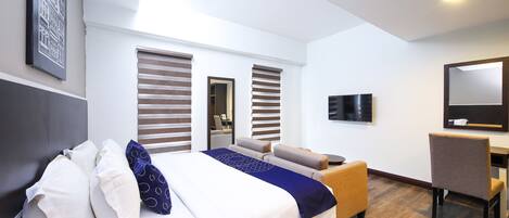 A hotel room with a bed, a desk, a chair, and a TV.