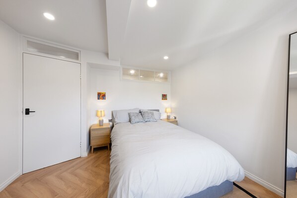 A bedroom with a large bed, two bedside tables with lamps, a wardrobe, and a ceiling light fixture.