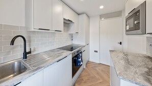 A modern kitchen with white cabinetry, a stainless steel sink, a built-in oven, and a microwave.