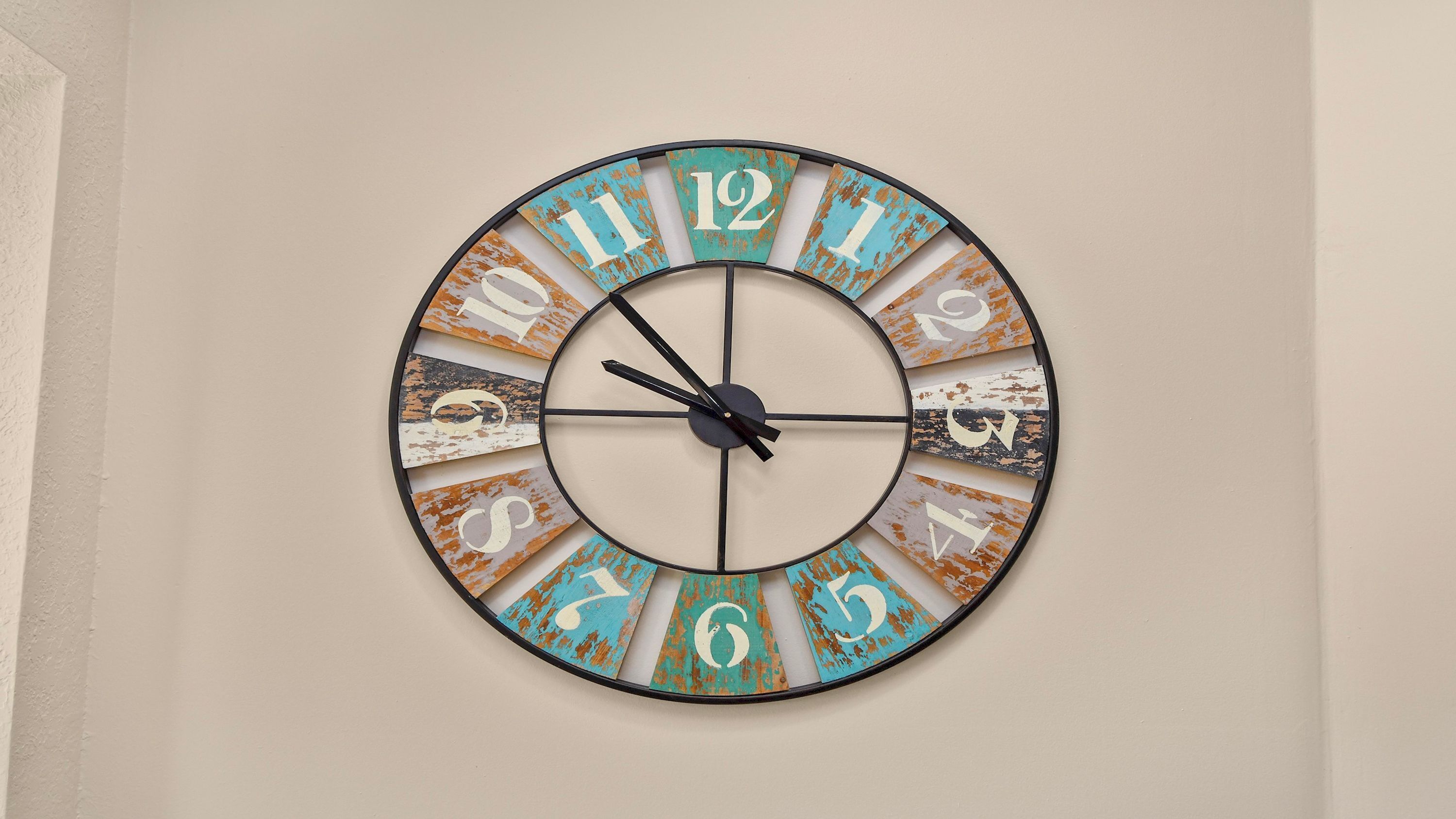 A circular wall clock with a rustic design, featuring numbers and letters in a distressed finish.