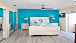 Ein Schlafzimmer mit einem Bett, zwei Nachttischen, einem Deckenventilator und einem großen Spiegel.