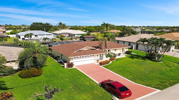 A residential area with houses, a red car parked in front of a house, and a well-maintained lawn. - Just Chill Modern Canal Villa w Heated Pool (Cape Coral)