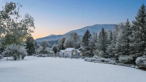 Ett snötäckt landskap med en rustik ladugård och träd.