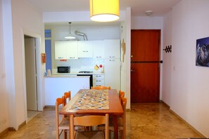 Une cuisine compacte avec des meubles blancs, un four à micro-ondes et une cuisinière. On aperçoit une table à manger avec des chaises au premier plan.