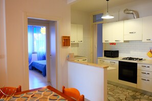 Une cuisine compacte avec des meubles blancs, un four à micro-ondes, une cuisinière et un petit coin repas comprenant une table et des chaises.