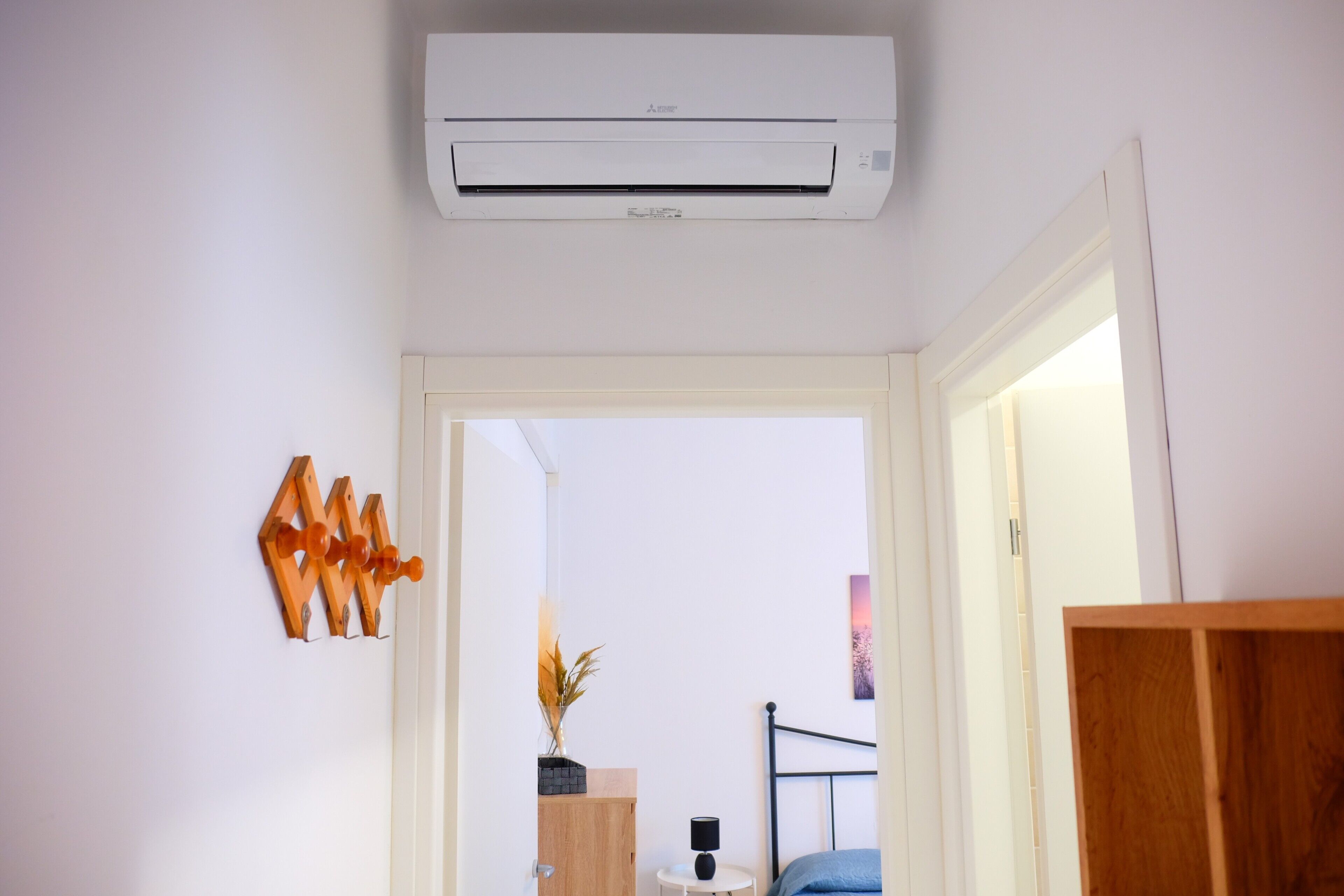 Un equipo de aire acondicionado instalado en el techo, un marco de puerta de madera y una pequeña mesa blanca con una lámpara.