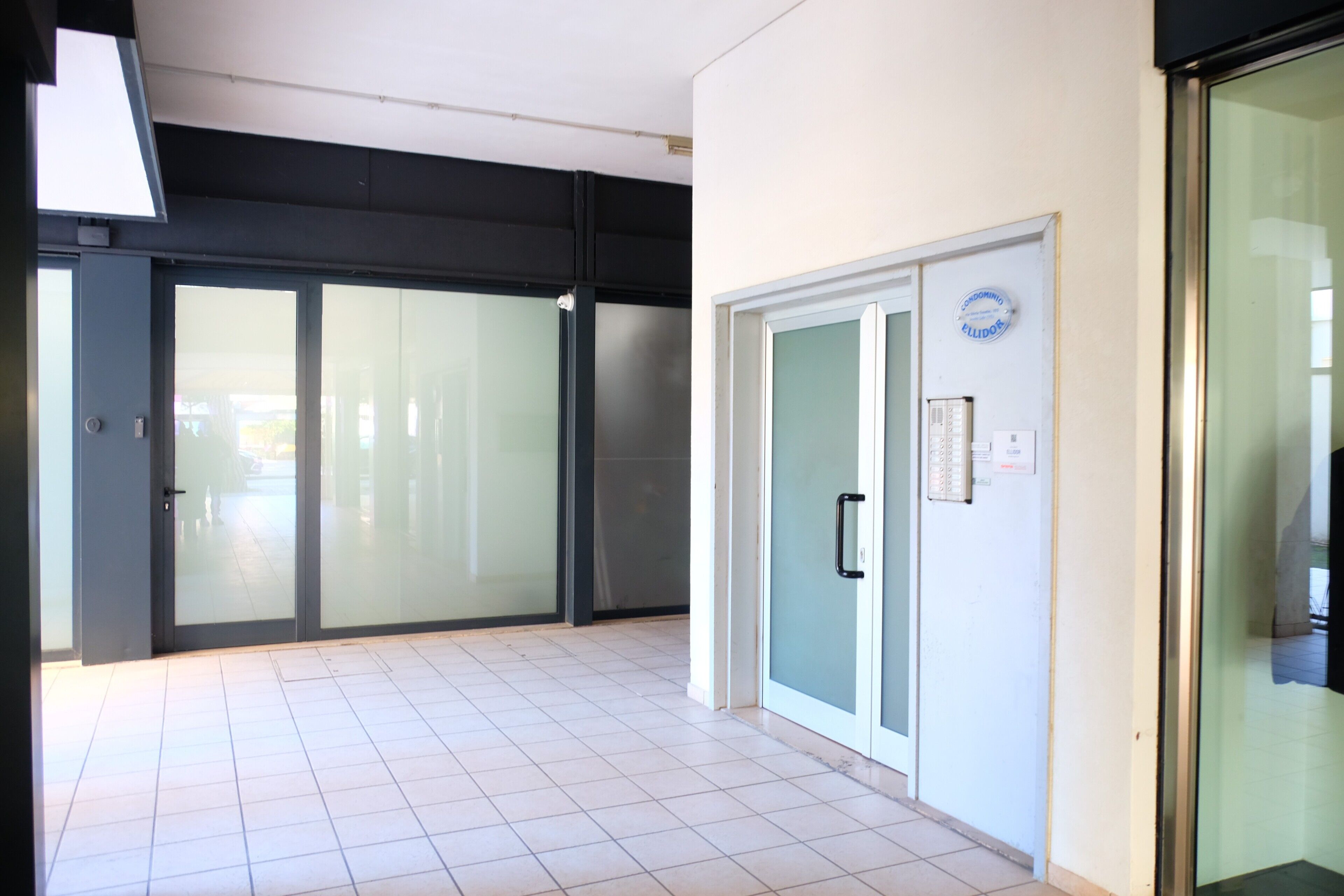 Un interior moderno con suelo de baldosas, una puerta de cristal con manija y un cartel en la pared.