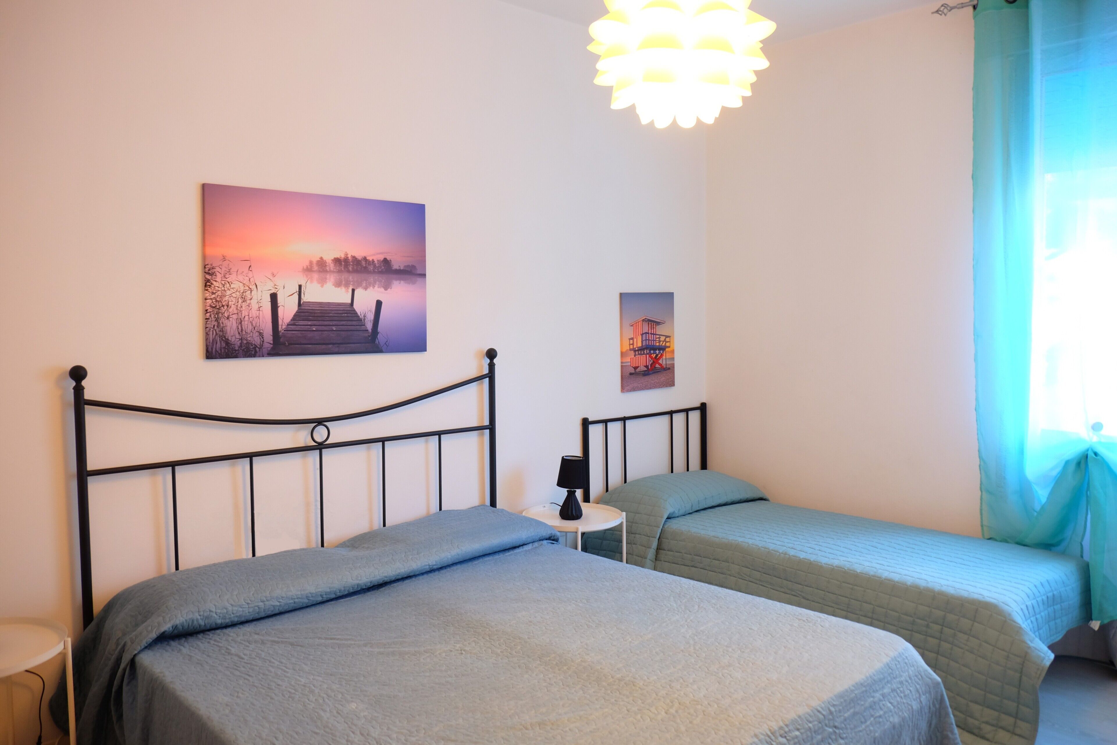 Un dormitorio con una cama, una mesita de noche, una lámpara y dos cuadros en la pared.