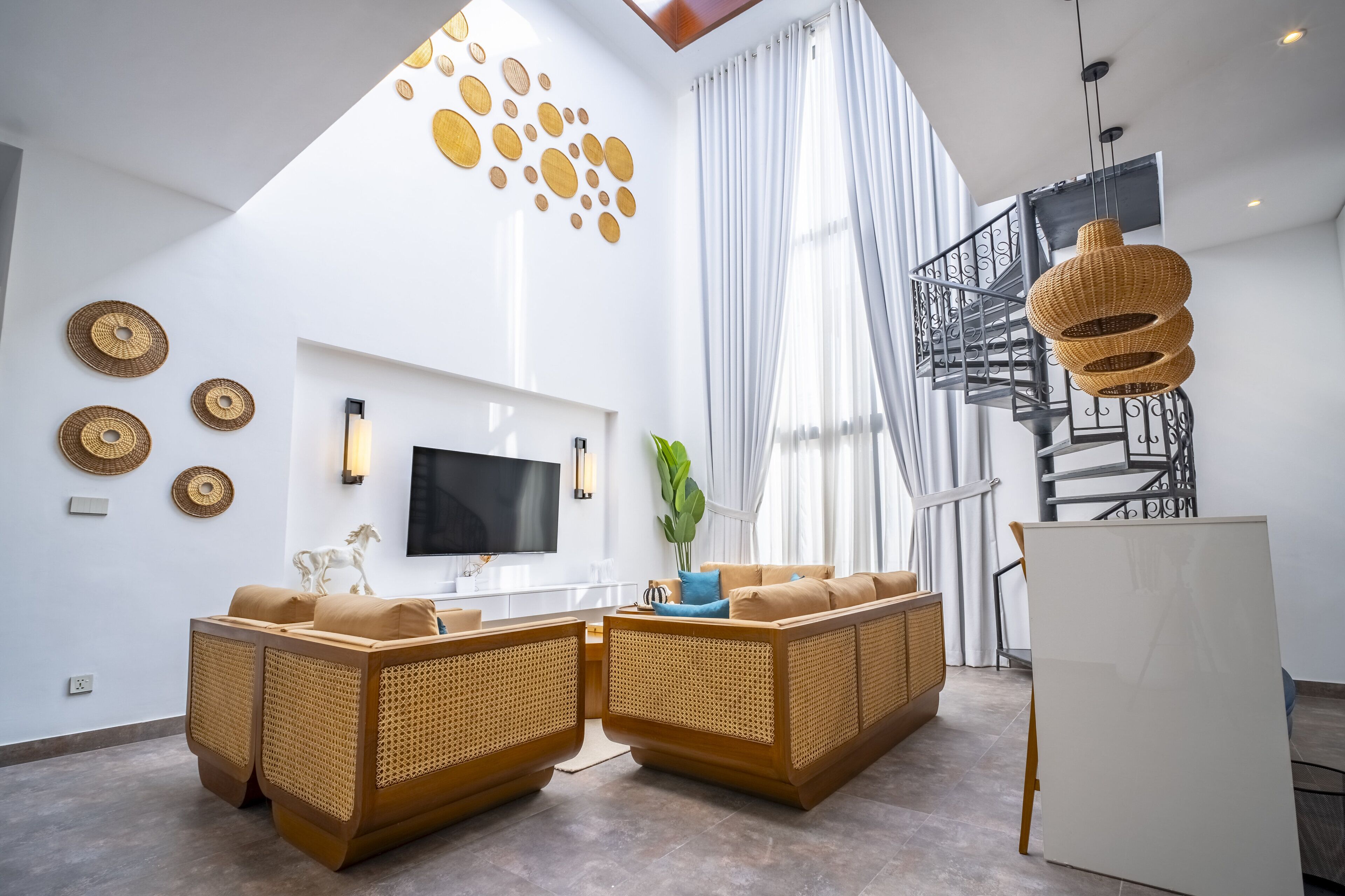 Una sala de estar moderna con un televisor grande, sofás de mimbre, una escalera y arte decorativo en la pared.