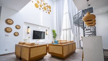 Una sala de estar moderna con un televisor grande, sofás de mimbre, una escalera y arte decorativo en la pared.