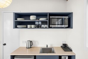 Una cocina compacta con microondas, estantes con platos, vasos y una tetera.