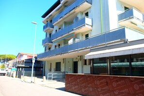 En bygning med flere etager, altaner, en overdækket indgang og en tydelig stueetage med et mønstret markise.