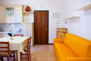 Ein Zimmer mit Esstisch, Stühlen, einer Couch, einer Holztür und einem kleinen Schrank.