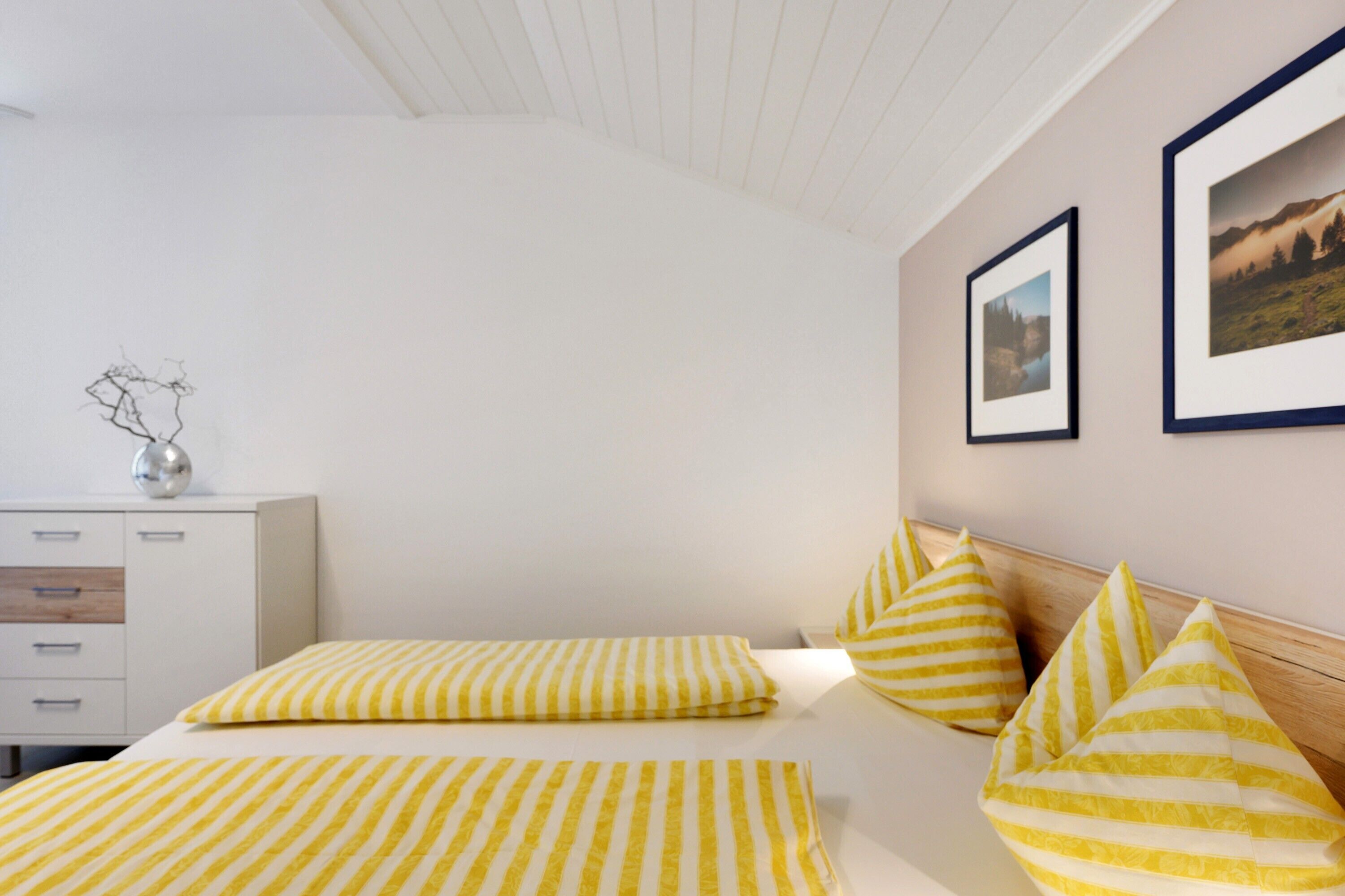 A bedroom with a bed, pillows, a dresser, and framed pictures on the wall.