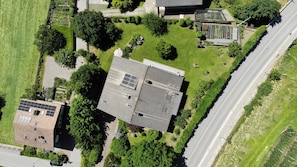 An aerial view of a residential area with a house featuring a sloped roof, solar panels, and a garden.