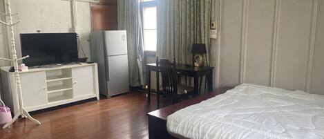 Et hotelværelse med seng, skrivebord med stol, fjernsyn, køleskab og aircondition.