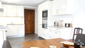 A modern kitchen with white cabinets, a wooden door, and a dining area with a wooden table set for two.