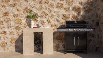 Una parrilla con un muro de piedra de fondo y una pequeña mesa con una planta y un objeto rojo.