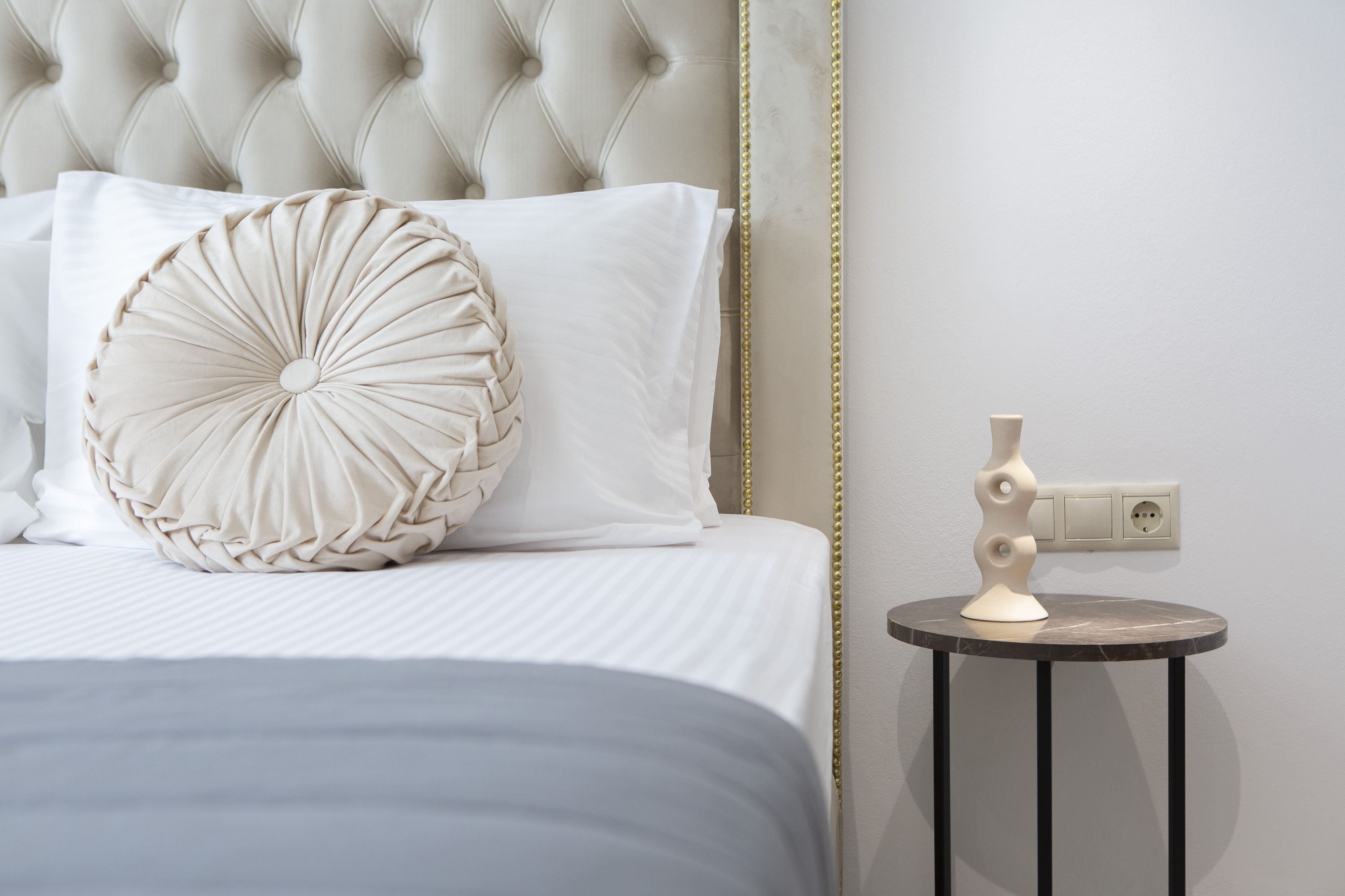 Uma cama bem arrumada com cabeceira estofada, um travesseiro decorativo e uma mesa de cabeceira com abajur.