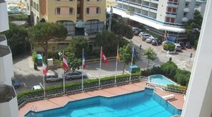 A pool area with multiple flags, a road with cars, and surrounding buildings.