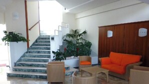 Eine Hotelhalle mit Treppe, Korbmöbeln, einem Holzschrank und Topfpflanzen.