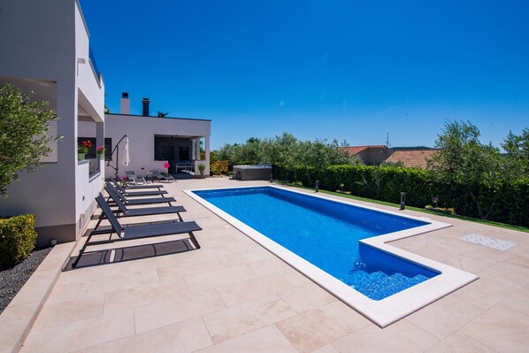 A modern pool area with a rectangular pool, lounge chairs, and a white building with a balcony. - Villa Bura Zadarvillas (Stankovci)
