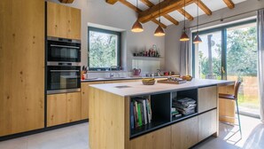 A modern kitchen with wooden cabinets, built-in ovens, a central island with a sink, and pendant lighting. - Beautiful private villa for 6 guests with A/C, private pool, WIFI, TV and patio (Trequanda)