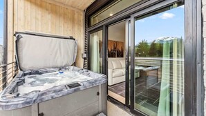 A hot tub with a wooden deck and a glass door leading to a patio area. - Alpine Nest Escape Su (Silverthorne)