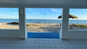 On peut admirer la plage depuis un espace abrité, avec un tapis bleu qui mène à la plage, un parasol en chaume et une chaise.