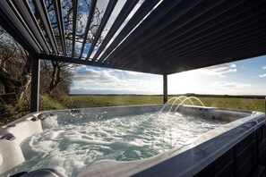 Un jacuzzi con vista a un campo verde y árboles bajo una pérgola.