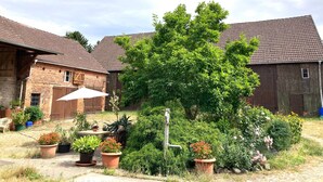 A rustic courtyard with brick buildings, potted plants, and a wooden table with an umbrella.
