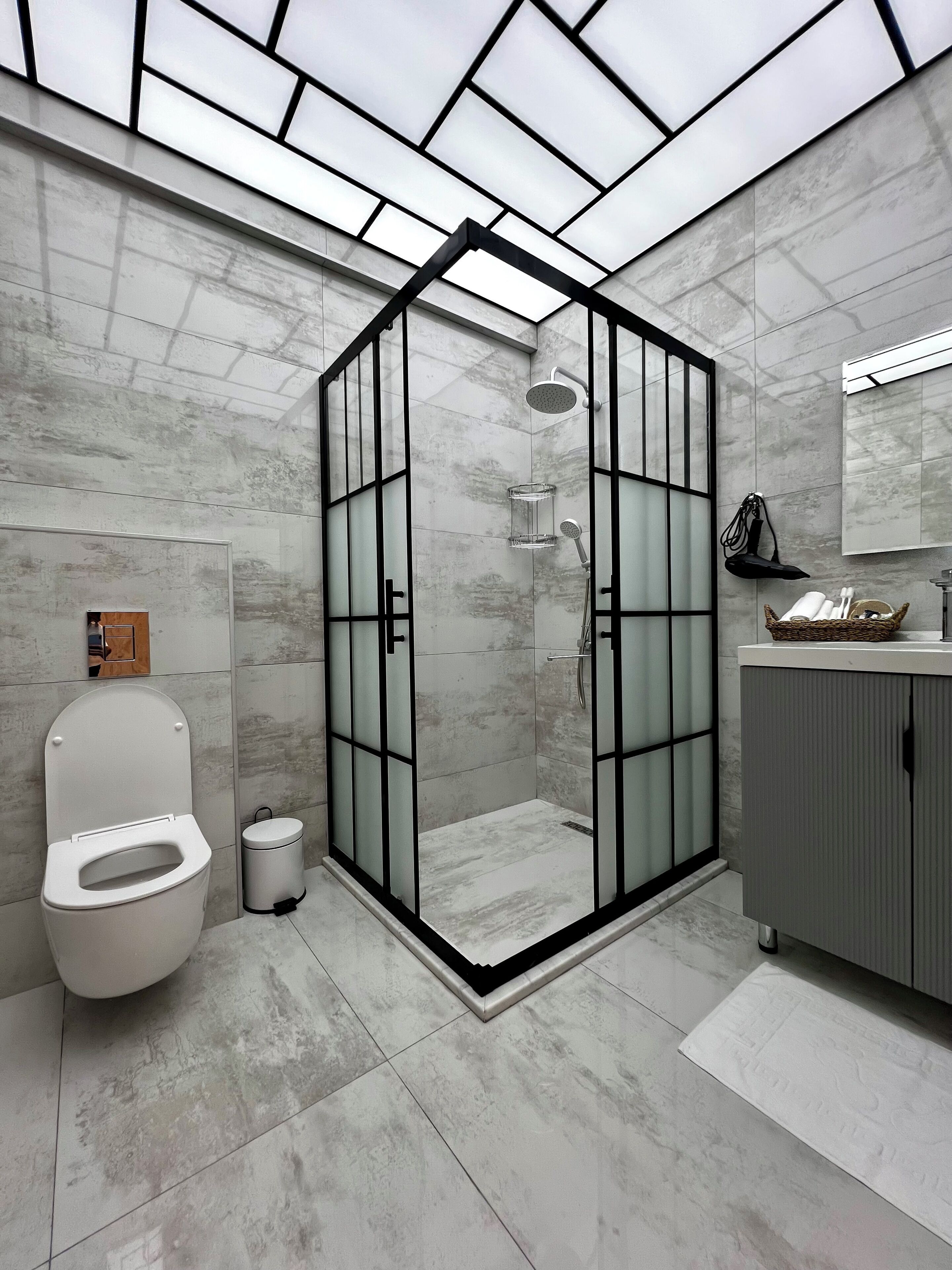 Ein modernes Badezimmer mit einer Duschkabine, einer Toilette, einem Mülleimer und einem Waschtisch mit Spiegel.