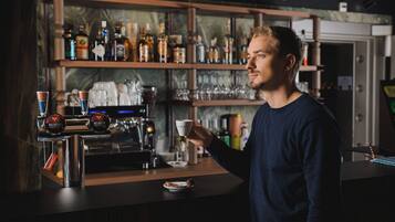 Una zona de bar con una máquina de café, estanterías llenas de botellas y una persona sosteniendo una taza.