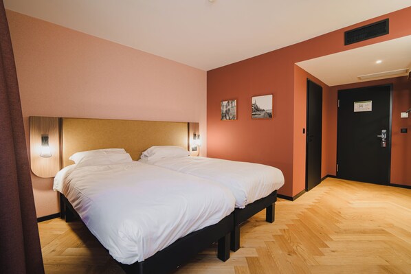 Una cama doble con ropa blanca, cabecera de madera, dos luces fijadas a la pared y piso de tablones de madera.