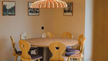 A dining area with a round wooden table and chairs, a hanging light fixture, and framed pictures on the wall.