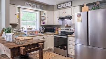 A kitchen with white cabinets, a stainless steel refrigerator, a microwave, and an oven. There is a window with a view of greenery outside.